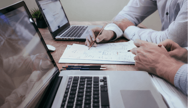 Hands writing notes next to an open laptop